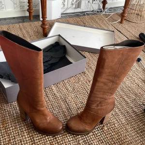 Bruna skinnstövlar från Vic - Snygga bruna skinnstövlar från Vic i mycket bra skick. De har en robust klack och dragkedja på sidan för enkel på- och avtagning. Perfekta för höst och vinter med sitt slitstarka material och stilrena design. Sulan har bra grepp för hala underlag.