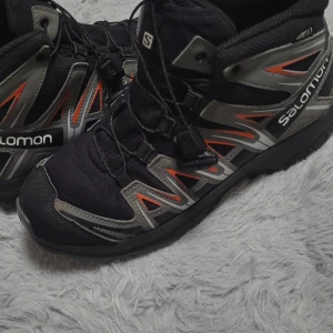 Svarta vandringskängor från Salomon - Säljer ett par robusta och bekväma svarta vandringskängor från Salomon. De har en snygg design med grå och orange detaljer och är perfekta för utomhusaktiviteter. Kängorna har snörning och är i mycket bra skick. Perfekta för höst- och vintervandringar! Även vinterskor sol håller värme jättebra. Skor i storlek 37.Använda ett par gången men har inga defekter alls och är väldigt fina. Nyköpt pris är 995kr. 