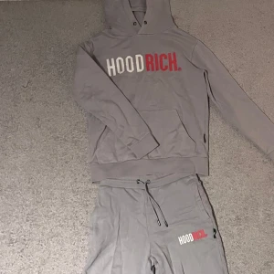 Hoodrich-set - Säljer en snygg grå hoodie och matchande byxor från Hoodrich. Hoodien har en stor ficka fram och texten 'HOODRICH' i vitt och rött på bröstet. Byxorna har fickor i midjan och samma text på benet. Perfekt för en avslappnad stil! Har av er vid minsta fundering 🤔| lämna gärna prisförslag✍️