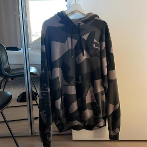 Gasp hoodie - Säljer en cool camouflage hoodie i svart och beige. Den har en stor ficka fram och justerbar huva med snören. Perfekt för en avslappnad stil och passar bra till vardag och gym. 
