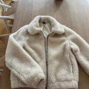 Vit teddyjacka med dragkedja - Mysig vit teddyjacka i mycket bra skick. Perfekt för höst o vår, Jackan har en dragkedja framtill och långa ärmar. Den är använd bara 2 gånger så den är i bra skick