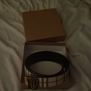 Rutig skärp från Burberry - Säljer ett snyggt Burberry skärp i klassiskt rutigt mönster. Storlek 115cm. Perfekt för att ge din outfit en lyxig touch. Kommer i originalförpackning. Passar både till vardag och fest!
