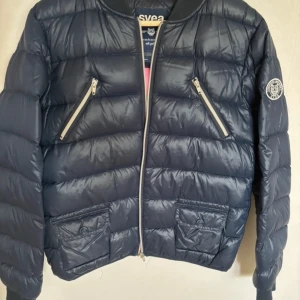 Svart dunjacka från Svea - Säljer en snygg svart dunjacka från Svea i mycket bra skick. Jackan har en stilren design med dragkedja framtill och två snedställda fickor med dragkedjor. Perfekt för kyliga dagar! 🖤