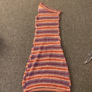 Randig oneshoulder klänning - Säljer en superfin randig klänning i härliga färger som lila, orange och rosa. Den är oneshoulder och har en tight passform som framhäver figuren. Perfekt för sommarens fester eller en dag på stan. Materialet är ribbat och stretchigt för extra komfort. Ett måste i garderoben för den som älskar färg och mönster!