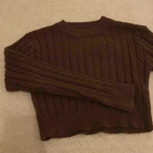 Brun stickad tröja - Säljer en mysig brun stickad tröja med kabelstickat mönster. Perfekt för kyliga dagar med sin varma och bekväma design. Tröjan har långa ärmar och en rund halsringning. Passar perfekt för svarta jeanse och för en liten myskväll ! 
