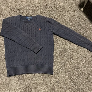 Mörkblå stickad tröja från Polo Ralph Lauren - Säljer en snygg mörkblå stickad tröja från Polo Ralph Lauren. Den har ett klassiskt kabelstickat mönster och den ikoniska loggan i röd på bröstet. Perfekt för både höst och vinter, passar till folk runt 150-160. Tvättad många gånger men i bra skick, 1500kr nypris. Skickar inom 1-3 dagar.