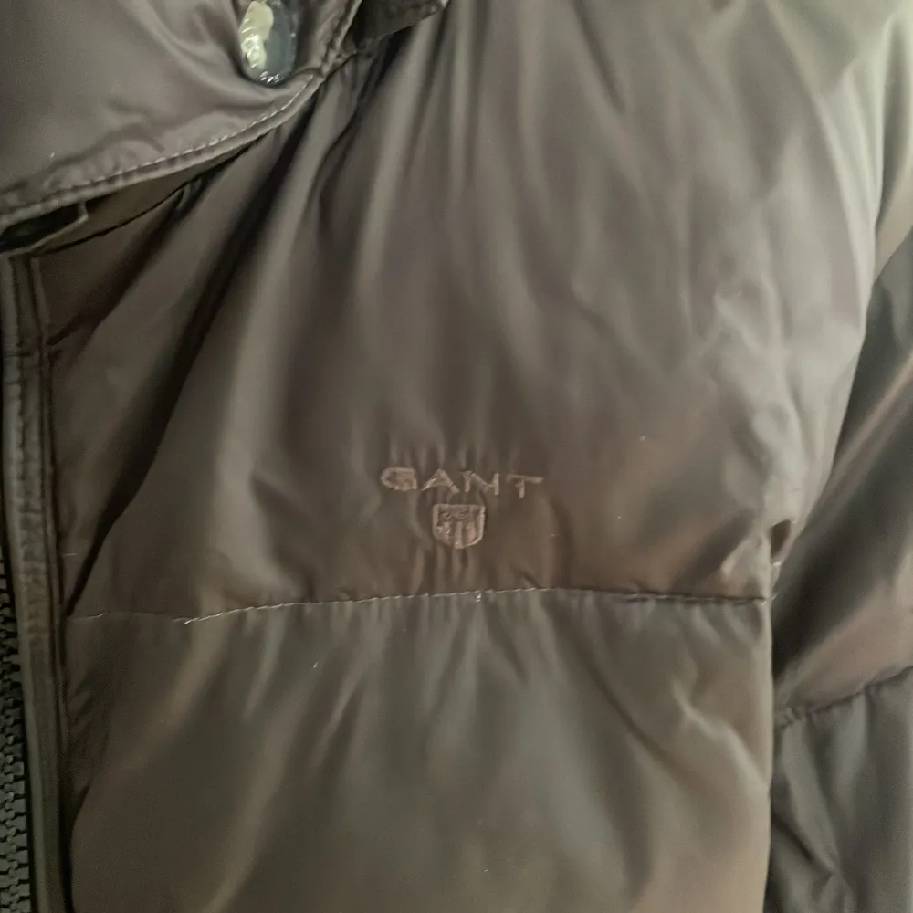 Säljer en snygg svart dunjacka från GANT i mycket bra skick. Jackan har en dragkedja framtill och en praktisk huva. Perfekt för kyliga höst- och vinterdagar. Den är långärmad och har en stilren design som passar till det mesta. Perfekt för dig som vill hålla stilen i kylan!. Takit.