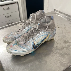 Grå Nike mercurial fotbollsskor  - Säljer ett par grå Nike fotbollsskor i bra skick. De har en cool design med färgglada detaljer och snörning. Perfekta för fotbollsträning eller match. Skorna har en tight passform och är gjorda i syntetmaterial för bästa prestanda på planen.