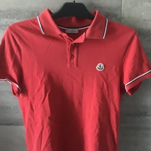 Röd pikétröja från Moncler - Säljer en snygg röd pikétröja från Moncler i bra skick. Den har korta ärmar och en klassisk krage med vita och blå detaljer. Perfekt för både vardag och fest! 🔥