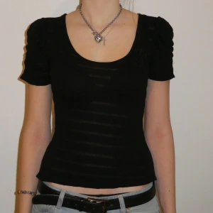 Svart, meshaktig topp - Svart topp med genomskinliga detaljer och en liten rosett. Perfekt till både fest eller skola. Storlek S. 