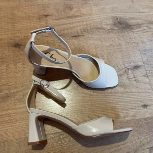  sandaler med klack från Clou - Snygga gräddvita klackskor från Clou i storlek 37. De har en elegant klack och en justerbar rem runt ankeln för perfekt passform. Skorna är i mycket bra skick! 