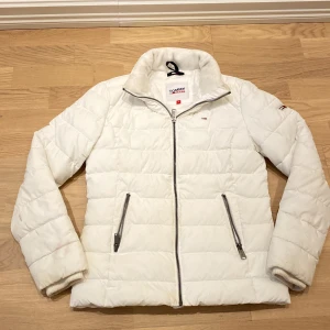 Vit quiltad jacka från Tommy Jeans - Säljer en snygg vit quiltad jacka från Tommy Jeans i storlek S. Jackan har en dragkedja framtill och två praktiska fickor med dragkedjor. Perfekt för kyliga dagar och ger en stilren look. Passar både till vardags och lite finare tillfällen. 🧥✨