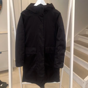 Svart kappa från Elvine - Säljer en svart kappa från Elvine i storlek XS. Den har en stilren design med dragkedja och knappar framtill. Perfekt för höst och vinter med sin varma vaddering. Jackan har långa ärmar och en praktisk huva för extra skydd mot väder och vind. Modellen heter ”allyson” och har ett nypris på 3800. Superfint skick!!! 