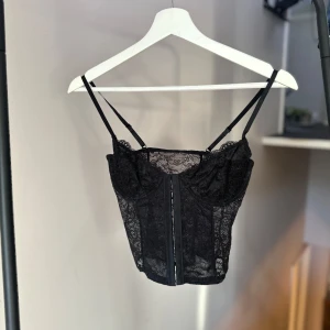 Svart spetskorsett NAKD - Snygg svart spetskorsett med smala axelband. Perfekt för en utekväll eller fest. Passar bra under en kavaj. Nyskick, endast provad! Nypris 349kr