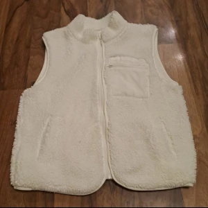  Teddy väst Lindex  - Mysig vit fleeceväst perfekt för kyliga dagar. Västen har en dragkedja framtill och en praktisk bröstficka. Den är i bra skick och passar perfekt för höst och vinter. Storlek 152-164cm
