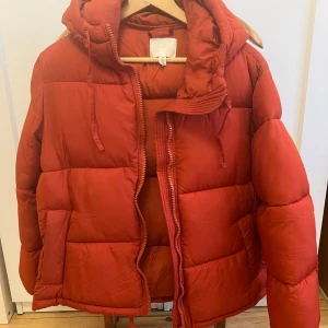 Röd/orange pufferjacka från H&M - Säljer en snygg röd/orange pufferjacka från H&M, storlek S i nyskick! Jackan har en mysig huva och dragkedja framtill. Perfekt för kalla vinterdagar!☃️