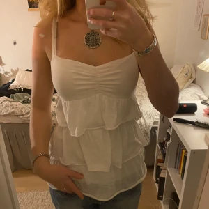 Vit volangtopp - Vitt linne med volanger, köpt secondhand och har därför vissa tecken på användning men funkar fortfarande fint🙌🏼 justerbara band
