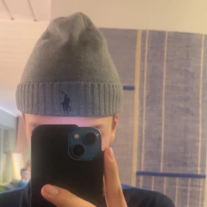 Grå mössa från Ralph Lauren - Säljer en snygg grå mössa från Ralph Lauren med ribbad kant och den klassiska loggan broderad framtill. Perfekt för kyliga dagar och ger en stilren look. Passar både till vardags och lite finare tillfällen. Den är i nästan perfekt skick och som ny kostar över 700kr.