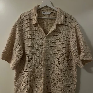 Beige stickad / virkad piké från Zara - Säljer en superfin beige stickad skjorta från Zara. Den har korta ärmar och ett snyggt mönster med hålstickning som ger en luftig känsla. Perfekt för sommarens varma dagar eller som ett lager under hösten. Skjortan är i mycket bra skick och passar både till vardags och fest! 🌟 Nyskick.