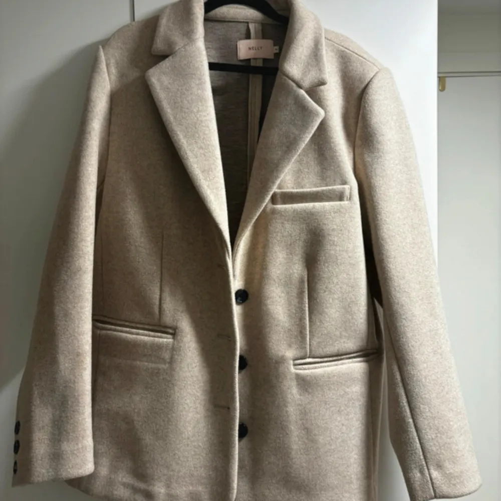 Säljer en stilren beige kappa från Nelly i mycket bra skick. Den har en klassisk design med knappar framtill och fickor på sidorna. Perfekt för höst och vår, och ger en elegant touch till vilken outfit som helst.. Takit.