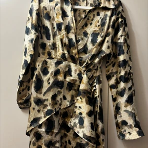 Leopardmönstrad omlottklänning - Snygg leopardmönstrad omlottklänning med långa ärmar. Perfekt för en utekväll eller fest! Klänningen har en cool knytning i midjan som ger en smickrande passform. Materialet känns lyxigt och bekvämt.