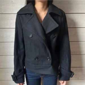 Svart kappa från Jackpot - Säljer en snygg svart kappa från Jackpot i mycket bra skick. Den har en dubbelknäppt design med stora knappar och långa ärmar. 60% ULL så jätte varmt 