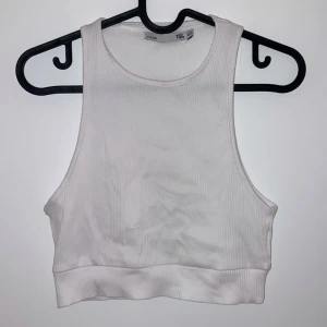 Vit ribbad linnetopp - Säljer en snygg vit ribbad linnetopp i storlek L. Perfekt för sommardagar eller som ett basplagg i garderoben. Toppen är ärmlös och har en croppad passform som ger en trendig look. Passar både till vardags och festliga tillfällen.