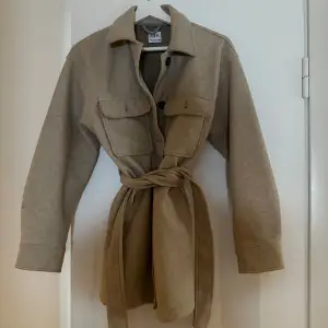 Säljer en snygg beige overshirt från Zara i mycket bra skick. Den har långa ärmar och knappar framtill samt ett bälte i midjan för en fin passform. Perfekt för höst och vår!