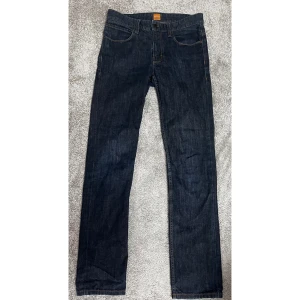 Mörkblå jeans från Hugo Boss - Säljer ett par snygga mörkblå jeans från Hugo Boss i bra skick. De har en klassisk straight passform och är perfekta för både vardag och fest. Jeansen har en stilren design med en läderpatch med Boss-märke på baksidan. Pris kan diskuteras