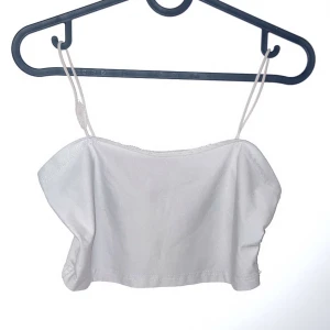 Vit axelbandslös topp - Snygg vit axelbandslös topp med smala axelband. Perfekt för sommardagar eller en kväll ute. Enkel och stilren design som passar till det mesta. Toppen är i ett lätt och bekvämt material.