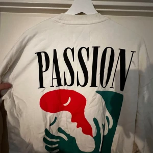 Vit sweatshirt från Vailent med tryck - Säljer en snygg vit sweatshirt  i storlek M. Tröjan har ett coolt tryck med texten 'PASSION' och en design i rött och grönt. Perfekt för en avslappnad stil eller att bära till vardags. Den är i bra skick och superbekväm! Kan mötas upp i Karlstad 