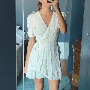 Linne klänning & Other Stories - En vit klänning med puffärmar och en v-ringning. Klänningen är i en wrap-stil och har en rosett i midjan.  Linne klänning