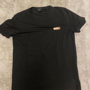 Svart t-shirt från Hugo Boss - Säljer en stilren svart t-shirt från Hugo Boss. Den har en slim fit passform och är gjord i ett material som hanterar fukt bra. T-shirten har korta ärmar och en liten metallbricka med Boss-loggan på bröstet. Perfekt för både vardag och fest!