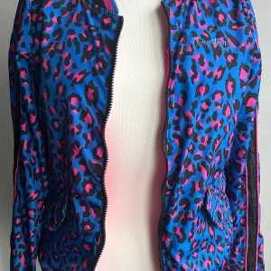 Färgglad jacka från Cars Jeans - Säljer en supercool jacka från Cars Jeans med ett unikt leopardmönster i blått och rosa. Jackan har en dragkedja framtill och är långärmad. Den är vändbar med en sida i helrosa med ett snyggt broderi av en tiger på bröstet. Perfekt för att sticka ut i mängden!