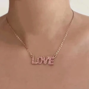 Halsband - Säljer ett superfint halsband med en berlock som stavar 'LOVE'. Halsbandet är i en vacker guldton och bokstäverna är täckta med glittriga stenar som verkligen fångar ljuset. Perfekt för att ge en extra touch av kärlek till din outfit! 💖Aldrig använt.