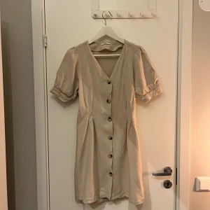 Linneklänning  - En fin beige linneklänning med knappar framtill och puffärmar.