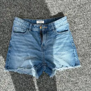 Säljer ett par snygga jeansshorts från Lindex i storlek EUR 158 / UK 12-13Y. De är i en klassisk blå denimfärg med fransiga kanter för en cool look. Shortsen har en dragkedja och knapp framtill samt fickor både fram och bak. Perfekta för sommardagar!