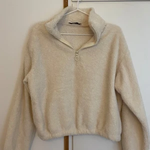 Beige fleece tröja från Chiquelle - Mysig beige lurvig tröja från Chiquelle i storlek XS. Perfekt för kyliga dagar nu på hösten. Tröjan har en halv dragkedja framtill och en hög krage för extra värme. Den är långärmad och är något kortare med resår nertill.