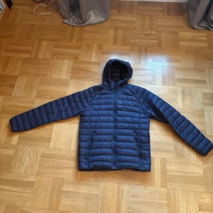 Mckinley Jacka  - Blå. Denna jacka är tillverkad i vind- och vattenavvisande material med PFC-fri impregnering. Vadderingen i polyester ger bekväm värme i kyligare och ruskigare väder. Jackan har tunna, elastiska band i ärmslut och nederkant för god passform. 