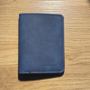Grisch mocka plånbok  - Säljer en stilren blå plånbok i skinn. Den har flera kortfack och en genomskinlig ficka för ID eller foto. Perfekt för att hålla ordning på dina kort och kontanter.