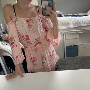 Ljusrosa blommig byxdress - Säljer en supersöt byxdress med blommor och spetsdetaljer. Den är öppen i axlarna och har anpassningsbara band. Resor i midjan ger en fin passform.   Säljer då den inte kommer till användning.