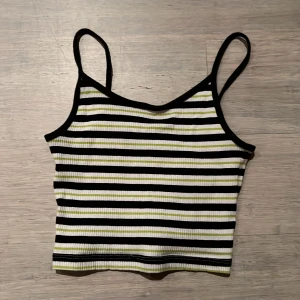 Randig ribbad linne - Säljer en superfin randig linne med smala axelband. Den är ribbad och har ett mönster i svart, vitt och grönt. Perfekt för sommardagar eller att ha under en jacka. Den är i bra skick och väldigt bekväm att ha på sig. Säljs inte längre!