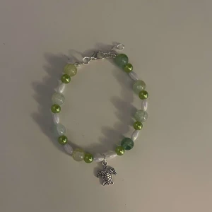 Färgglatt armband med elefantberlock - Säljer ett superfint armband med pärlor i olika gröna och vita nyanser. Armbandet har en söt liten elefantberlock i silverfärg som hänger i mitten. Perfekt för att ge lite färg till din outfit!