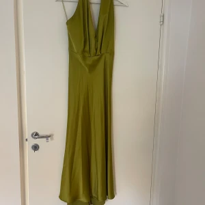 Olivgrön satinklänning  - Olivgrön/rostgul satinklänningmed halterneck. Knappar i nacken och vadlång 