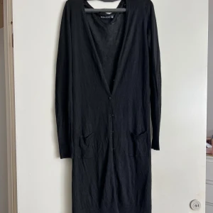 Svart lång kofta från Bershka - Säljer en svart lång kofta från Bershka. Den är stickad och har en v-ringad design med knappar framtill. Perfekt för höst och vinter, och den har praktiska fickor. Koftan är i nyskick och redo för en ny ägare!
