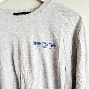 Grå långärmad tröja från PrettyLittleThing - Säljer en grå långärmad tröja från PrettyLittleThing. Den är supermjuk och perfekt för en avslappnad look. Tröjan har en enkel design med en liten logga på bröstet. Perfekt för höst och vår!