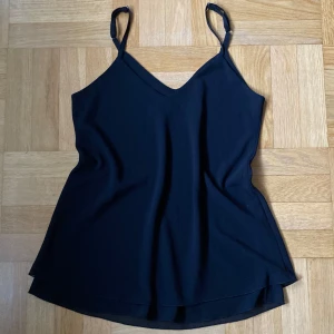 Svart linnetopp från Altamira Milano - Svart linne från Altamira Milano med smala justerbara axelband och volang-detalj längst ner!