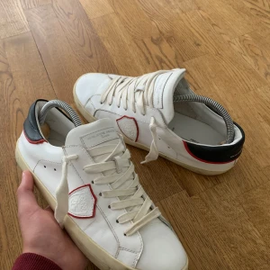 Vita sneakers från Philippe Model - Säljer dessa riktigt feta sneakers från Philippe model. Skorna är nästan helt oanvända. Skorna har en cool design med svarta och röda detaljer. De är i skinn och har snörning framtill. ( medföljer Philippe Model skor) kontakta mig vid mera frågor.