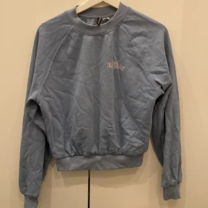 Blå sweatshirt från Divided - Säljer en snygg ljusblå sweatshirt från Divided. Den har en avslappnad passform med långa ärmar och ribbade muddar vid ärmslut och nederkant. Perfekt för en chill dag eller att mysa i hemma. 💙