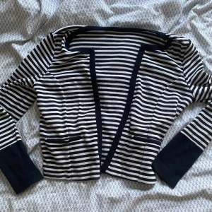 Randig svartvit cardigan - Säljer en snygg och stilren randig cardigan i mörkblå och vitt. Den har långa ärmar och två små fickor framtill. Perfekt för både vardag och festliga tillfällen. Passar bra till höst och vår!